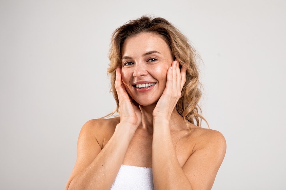 A woman smiling with her hands on her cheeks, showing the results of a broadband light treatment