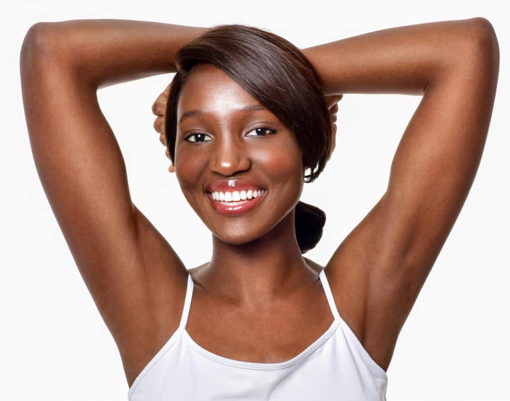 Beautiful young woman with dark skin, lifting her arms up to show off her smooth armpits after laser hair removal
